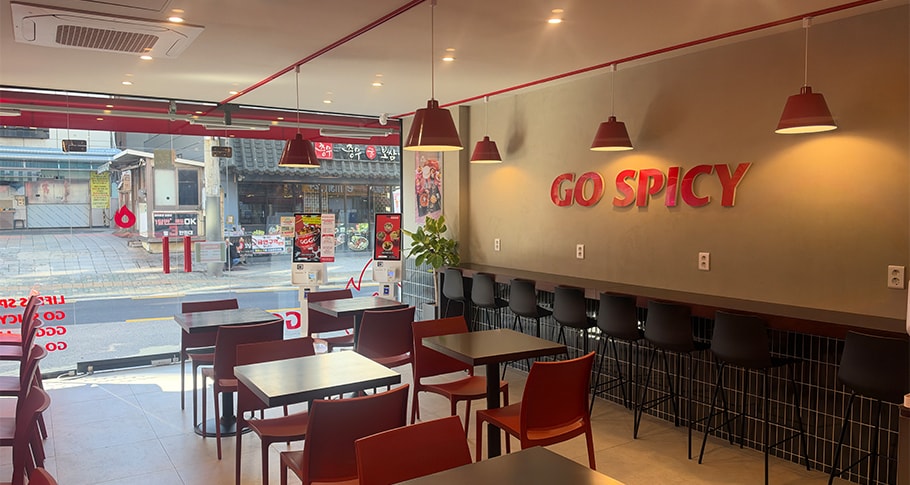 GO SPICY 벽 로고와 창가 좌석이 있는 지지고 매장 내부